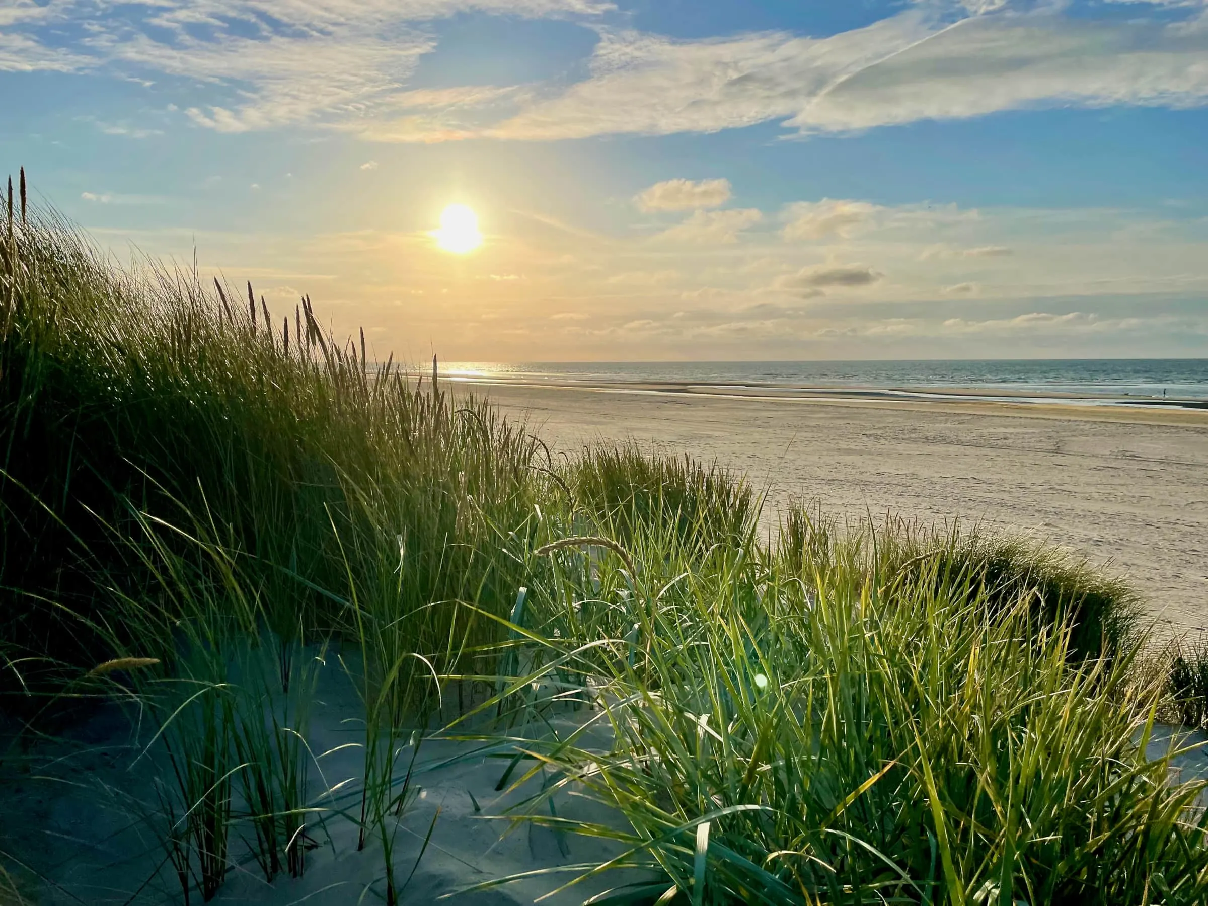 Ondergaande zon boven het strand, gezien vanaf de duinen bij Buren